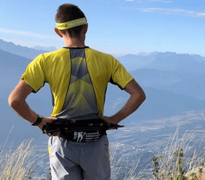 Sportif arrêté en haut d'une montagne, regardant le paysage. Il porte la running belt Sammie Trail